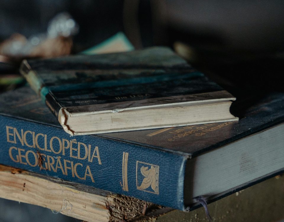 A close-up view of books, including an encyclopedia, resting on a rustic table in dim light.