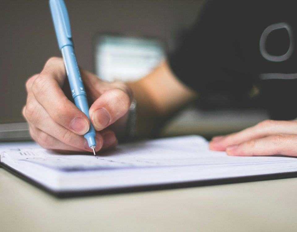 Close-up of hand writing in notebook using a blue pen, focus on creativity.