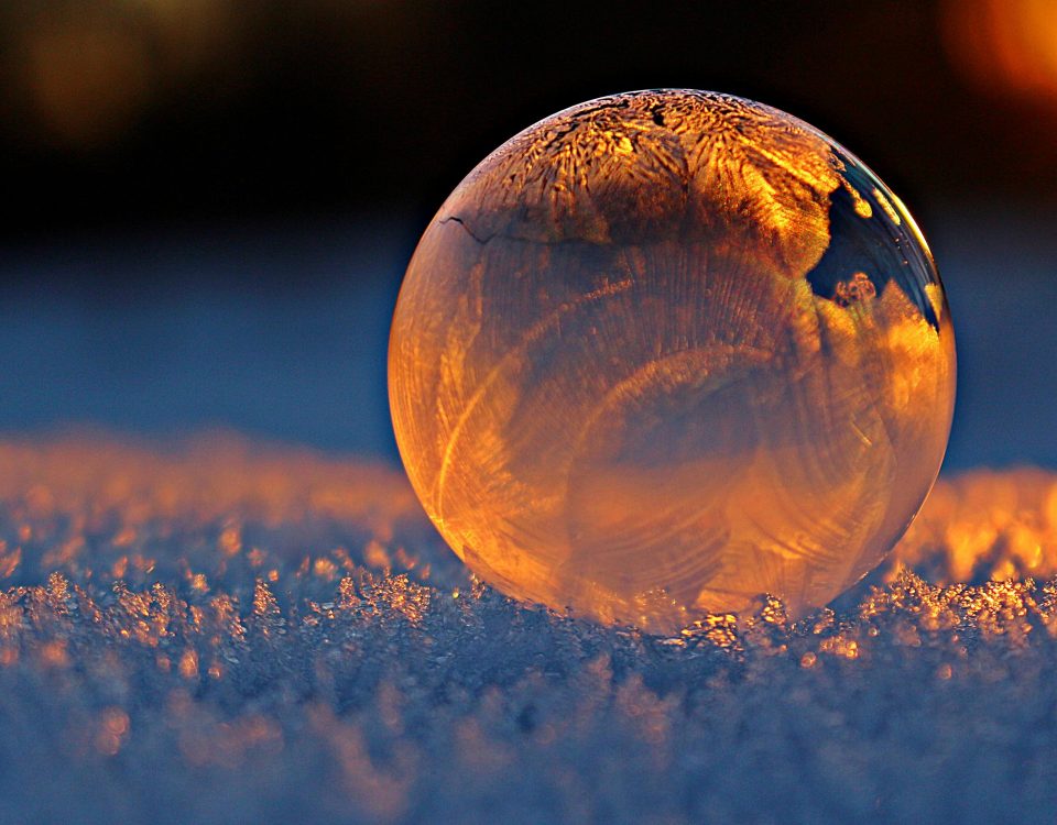 Close-up shot of a frozen bubble with warm reflections resting on a snowy surface at twilight.