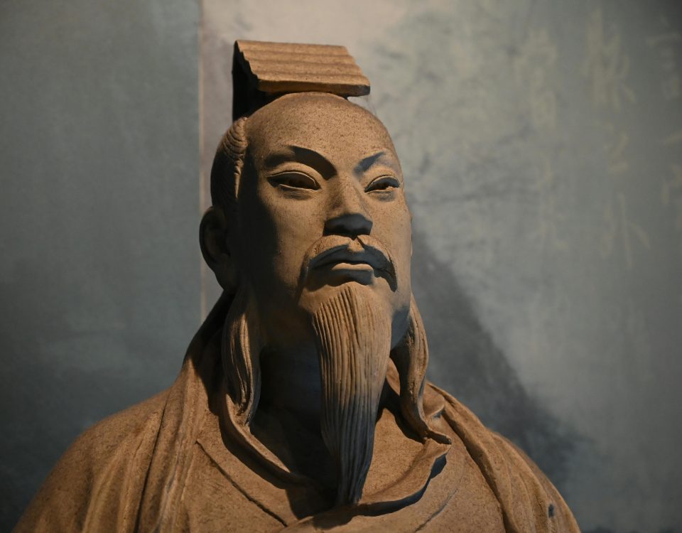 A detailed ancient statue of an Asian figure with traditional attire and expressive features.