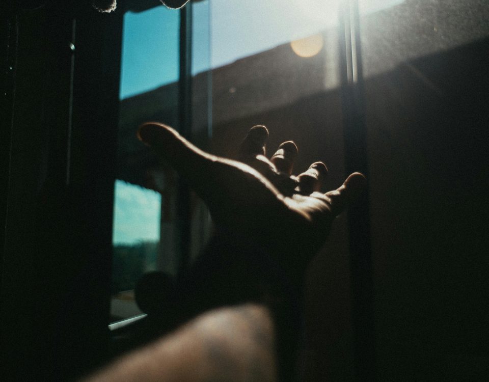 A dramatic portrayal of a hand reaching towards sunlight through a window, casting a shadow.