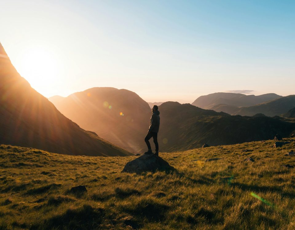 Silhouette of a person standing on a hill during sunrise in Cumbria, England with scenic mountain views.