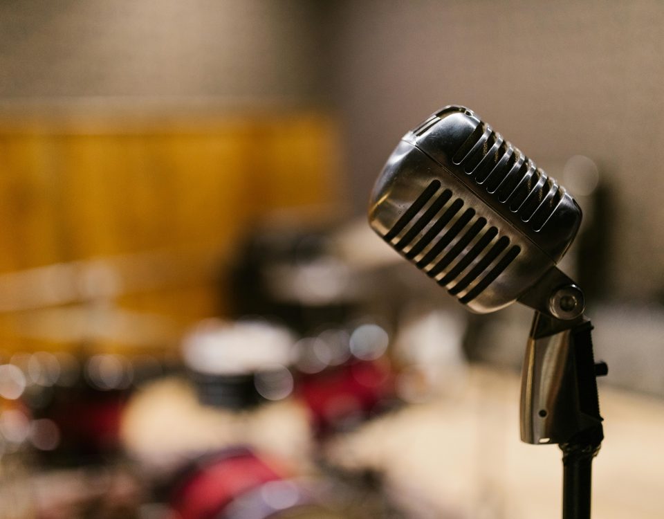 Close-up of a vintage microphone in a music studio with blurred drum set in the background.